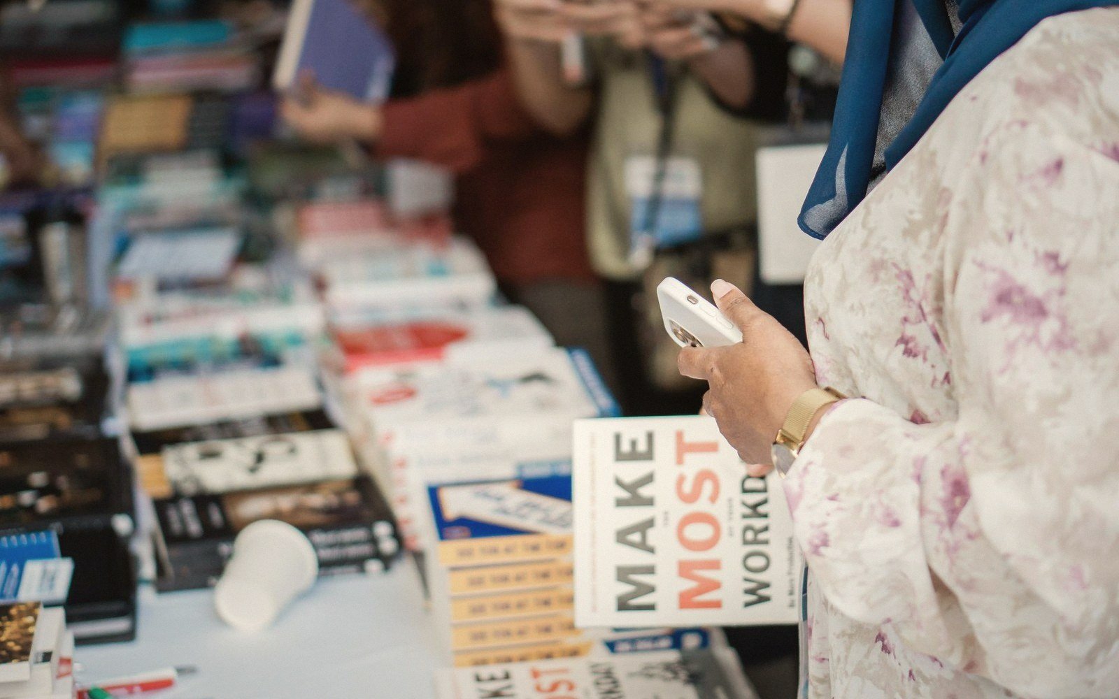 A woman browses a table of books, holding a smartphone and a paperback