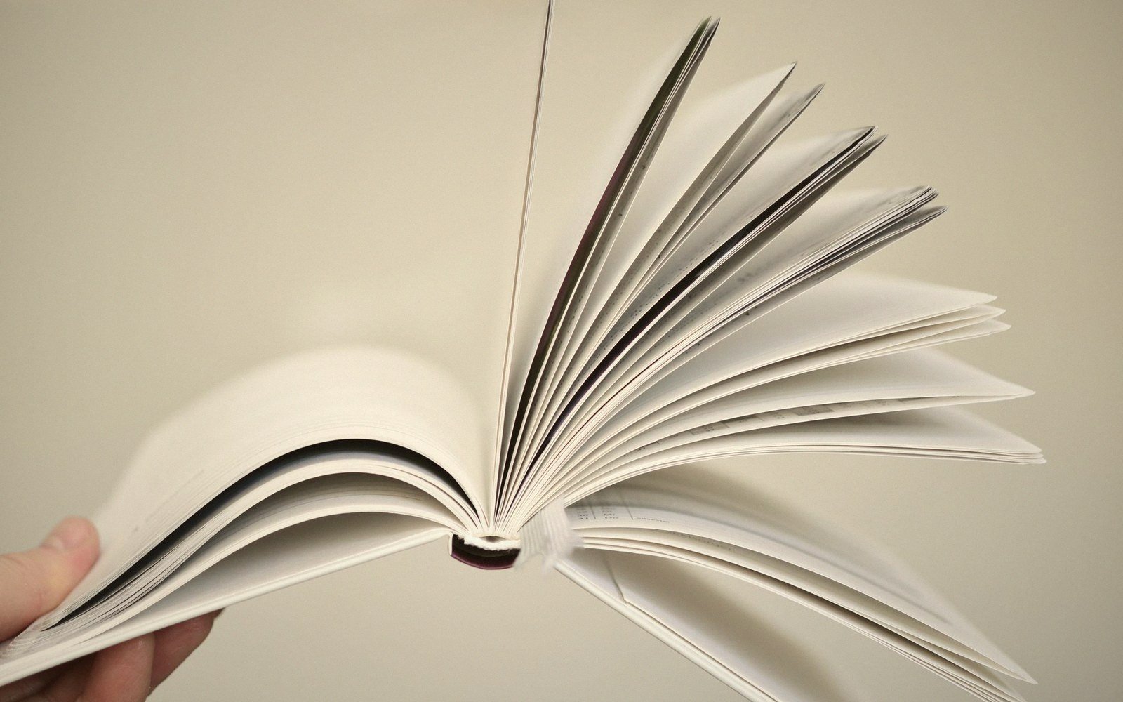 A hand holding an open book with pages fanned out mid-flip