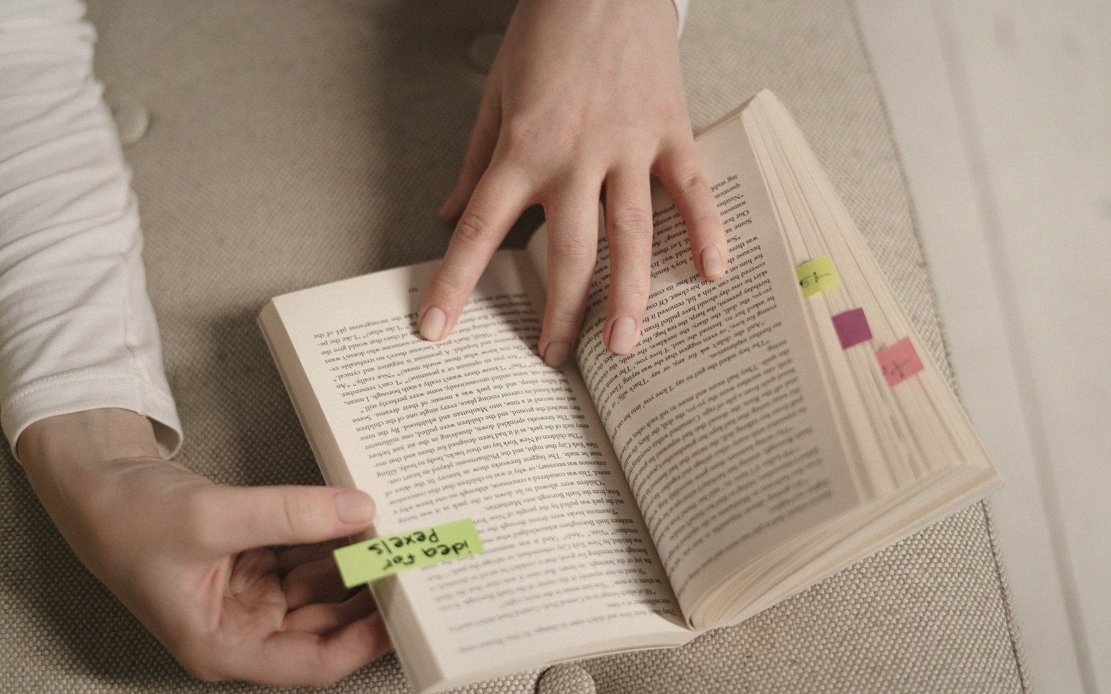 Hands placing colorful sticky note tabs while reading an open book