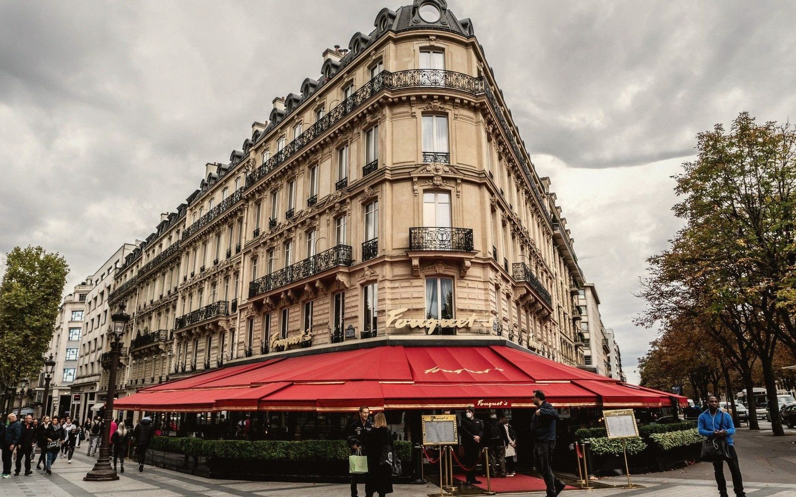 Fouquet's café with red awnings on a Parisian corner building, pedestrians passing by