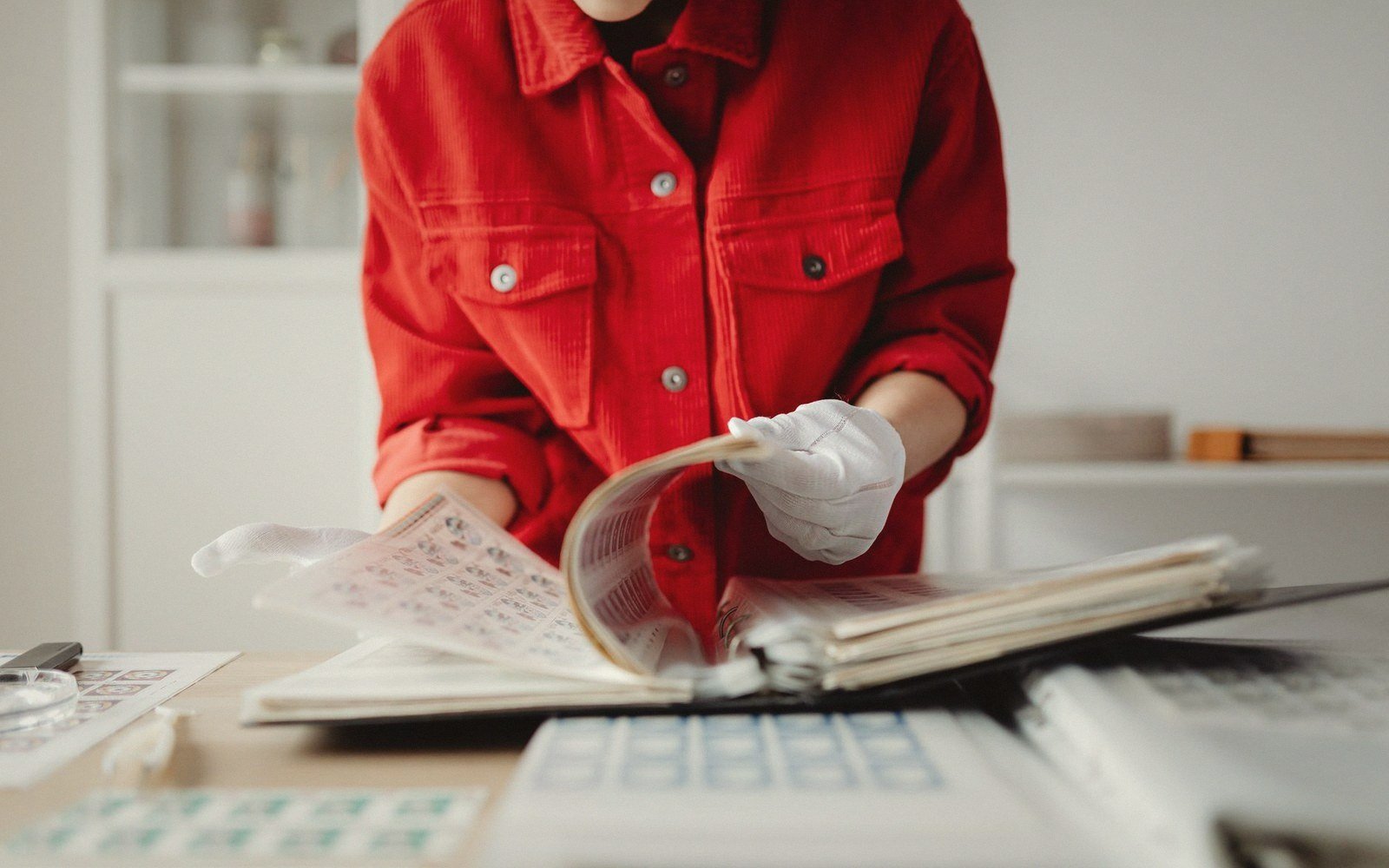 Person in white gloves turning pages of a stamp album on a desk