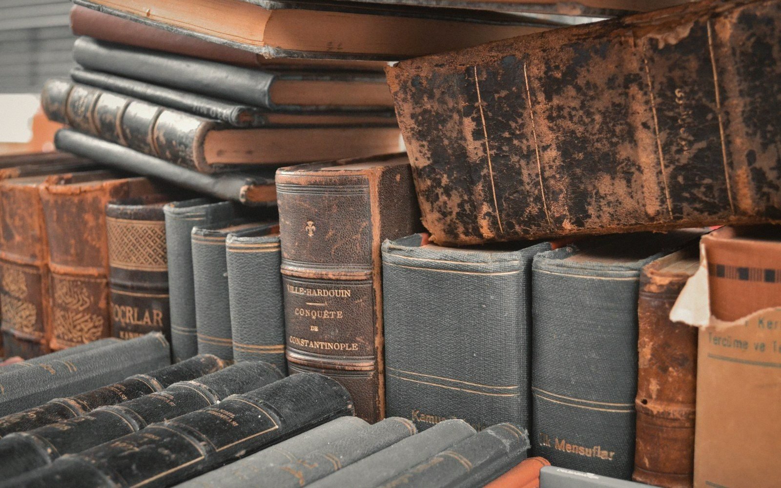 Worn leather-bound antique books stacked and shelved with faded gilt titles on spines