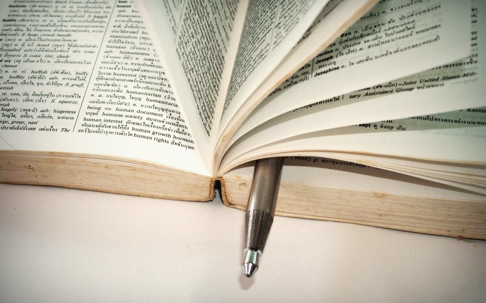 An open English-Thai dictionary with fanned pages and a pen resting between them