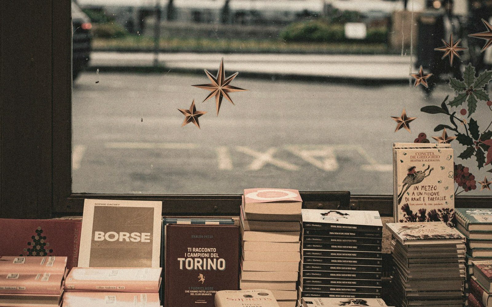 Stacked books in a shop window with star decals, facing a taxi lane outside
